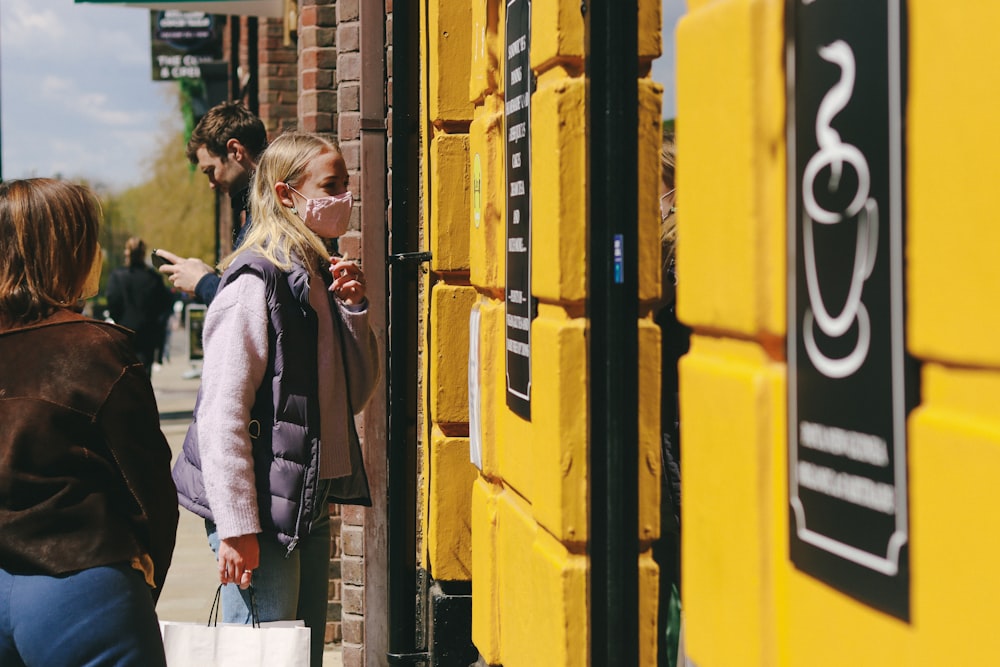 woman in gray coat standing beside yellow and black steel gate during daytime