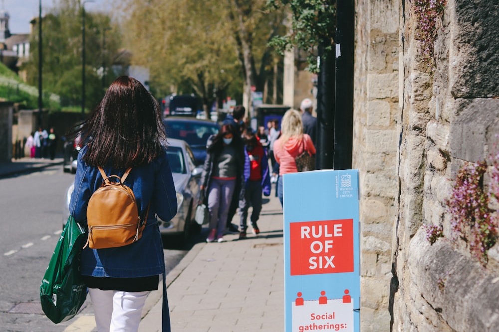 woman in brown jacket and white pants standing near white and blue signage