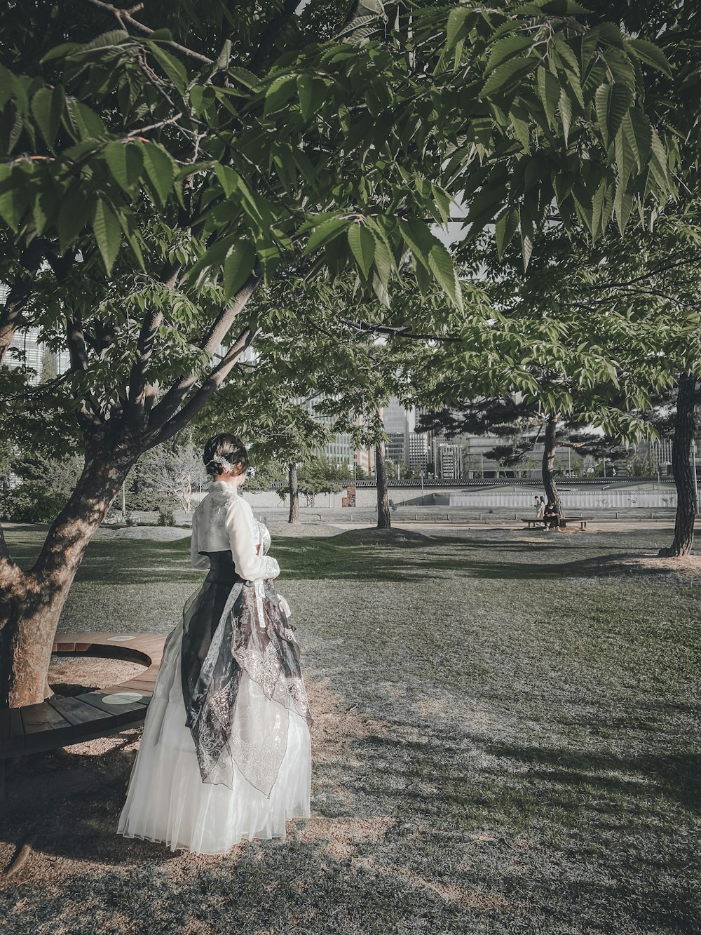 Mujer en vestido de novia blanco de pie bajo árbol verde durante el día