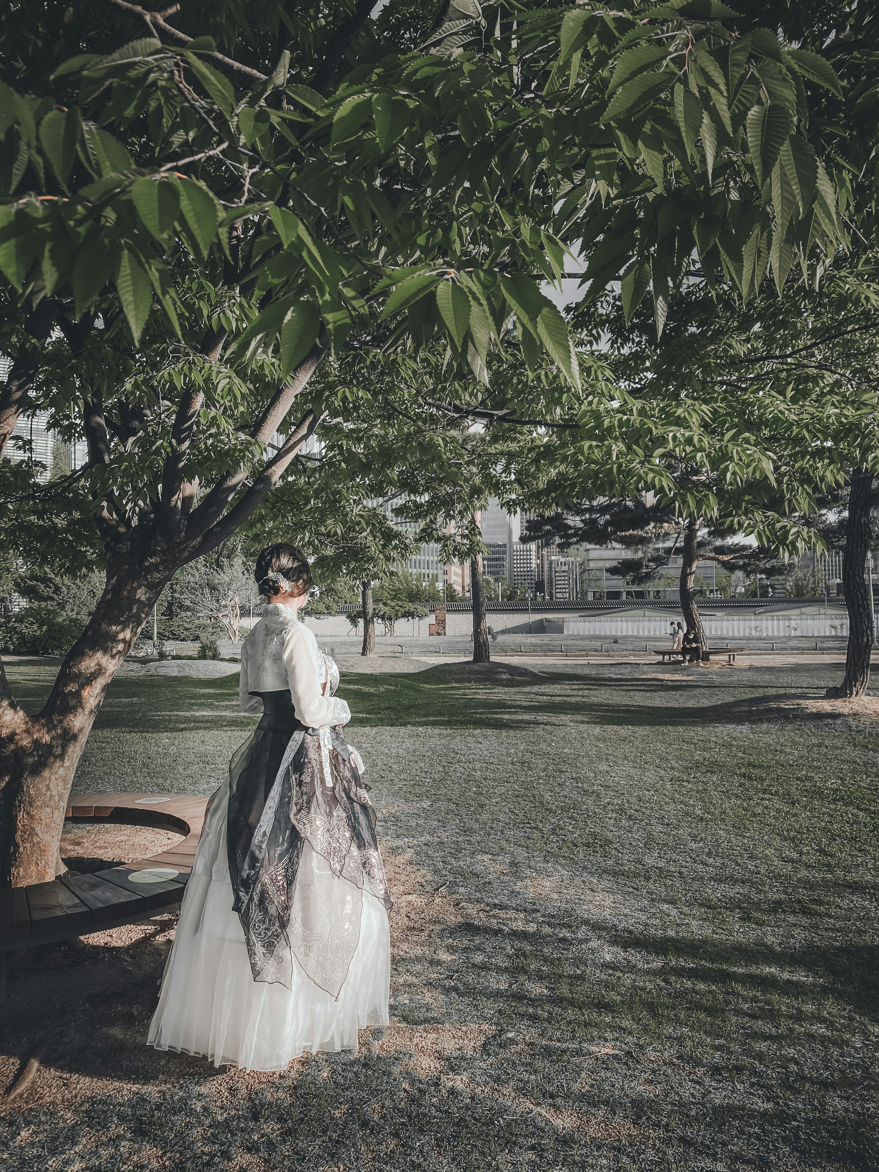 woman in white wedding dress standing under green tree during daytime