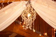 An inviting scene of the ballroom with black drapes, white feather accents, and twinkling fairy lights overhead.