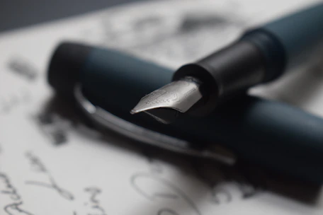 A close-up of a sleek brass and resin fountain pen resting on an elegant gift box with ink bottles nearby