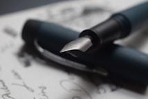 A close-up of a fountain pen resting on handwritten text, showcasing the intricate design of the pen's nib.