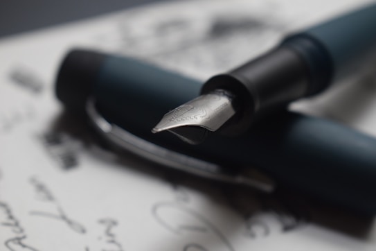 A close-up of a fountain pen resting on handwritten text, showcasing the intricate design of the pen's nib.