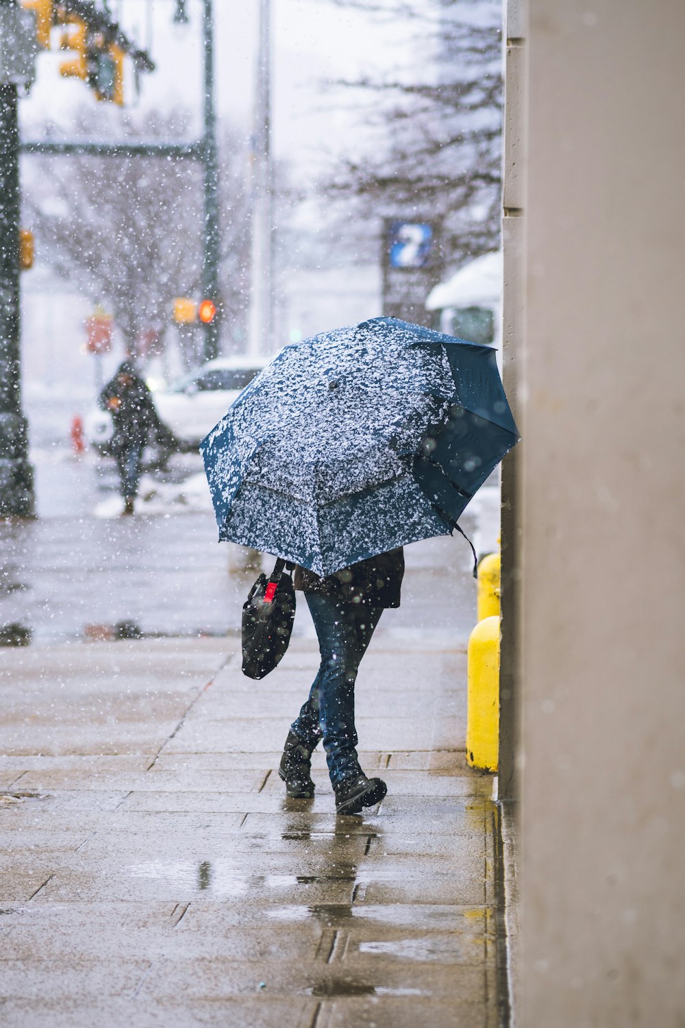 person in black jacket and black pants holding umbrella walking on wet road during rain