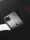 A smartphone with a sleek metallic finish, featuring a prominent logo and multiple camera lenses. It is positioned on a reflective dark surface with soft lighting creating a sophisticated ambiance.