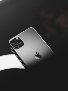 A smartphone with a sleek metallic finish, featuring a prominent logo and multiple camera lenses. It is positioned on a reflective dark surface with soft lighting creating a sophisticated ambiance.