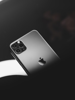 A smartphone with a sleek metallic finish, featuring a prominent logo and multiple camera lenses. It is positioned on a reflective dark surface with soft lighting creating a sophisticated ambiance.