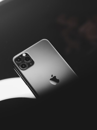 A smartphone with a sleek metallic finish, featuring a prominent logo and multiple camera lenses. It is positioned on a reflective dark surface with soft lighting creating a sophisticated ambiance.