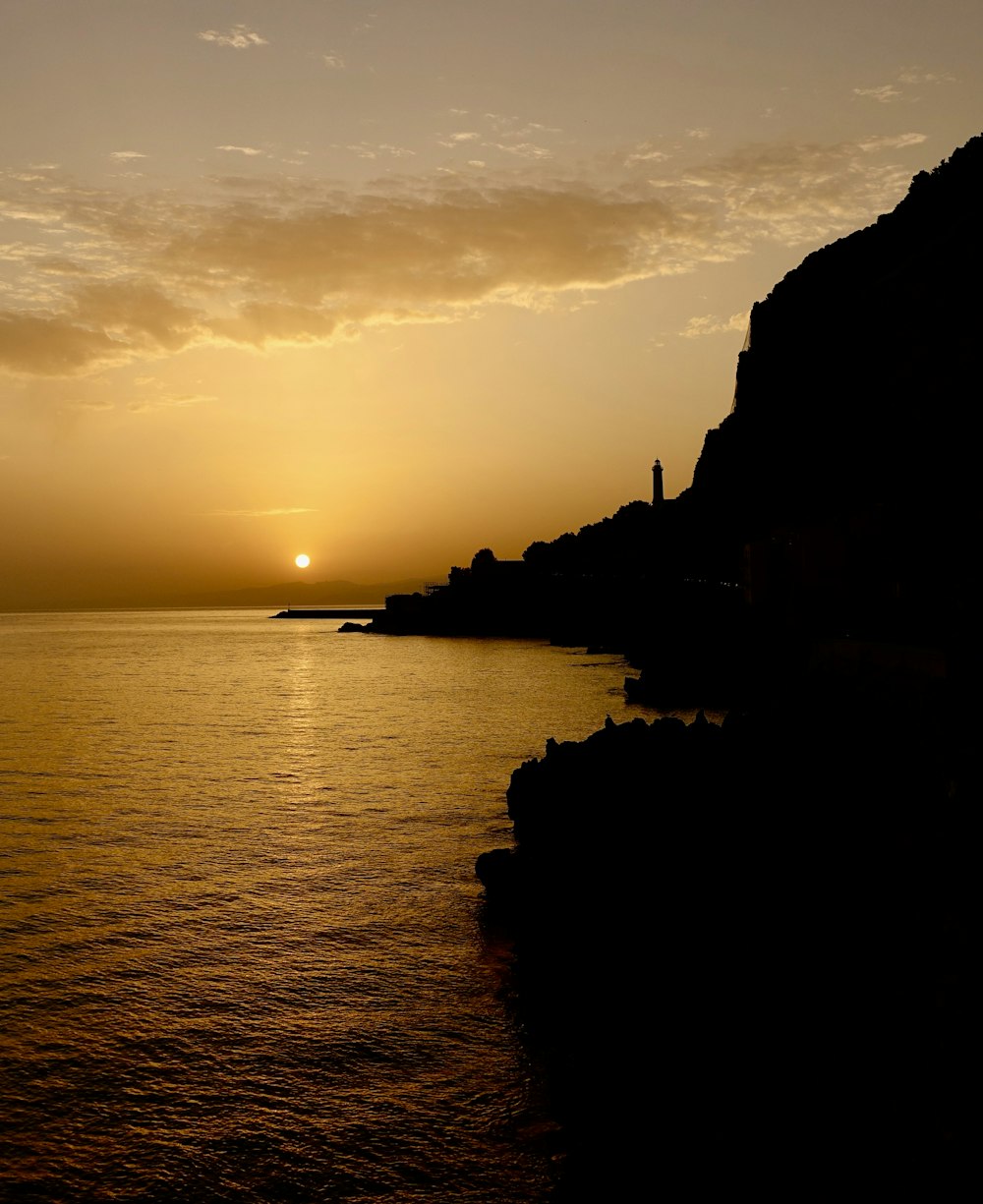 silhouette of rock formation on sea during sunset