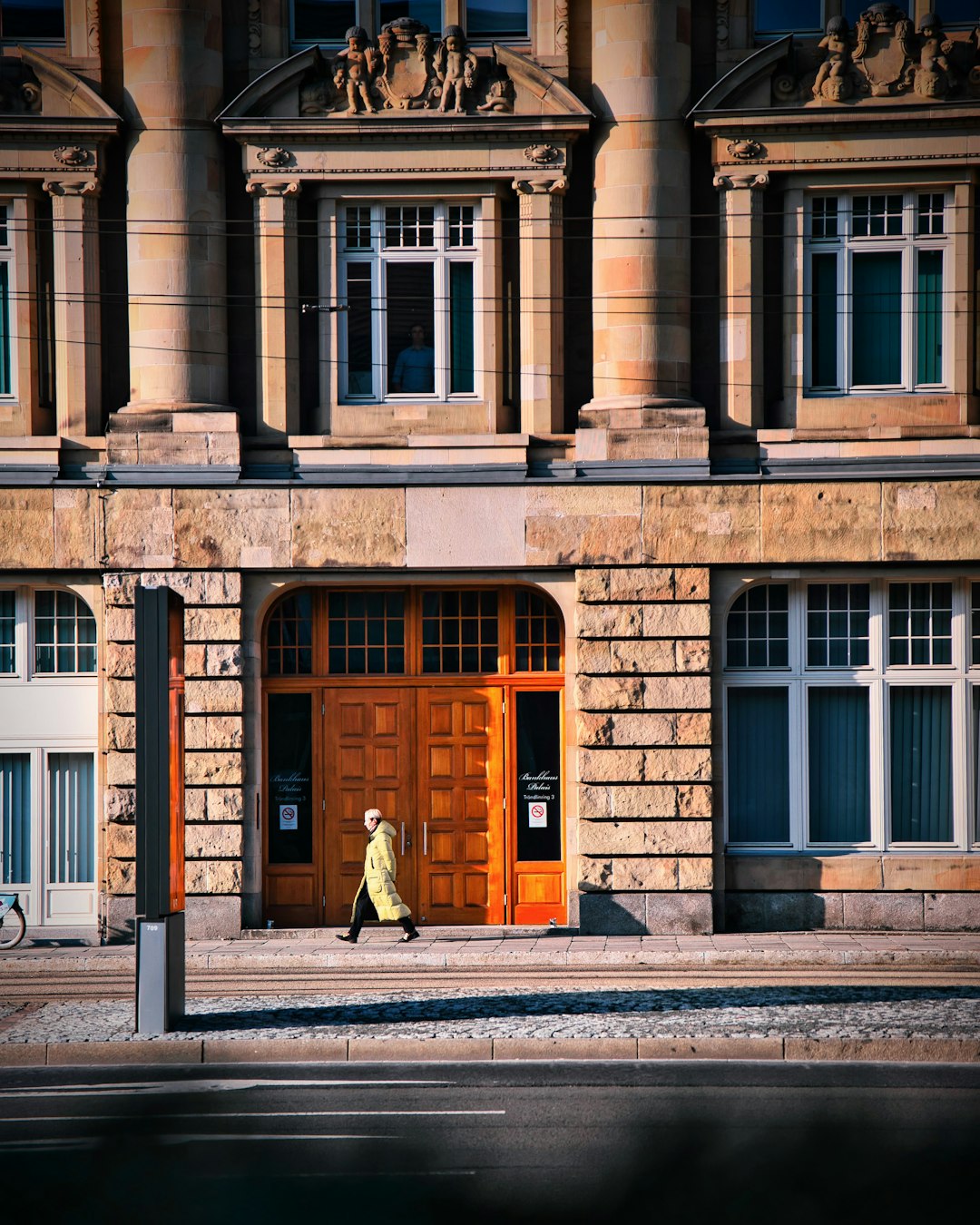 man in brown coat walking on sidewalk near brown concrete building during daytime