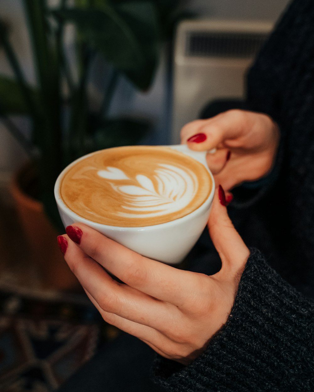 Person, die eine weiße Keramiktasse mit brauner Flüssigkeit hält