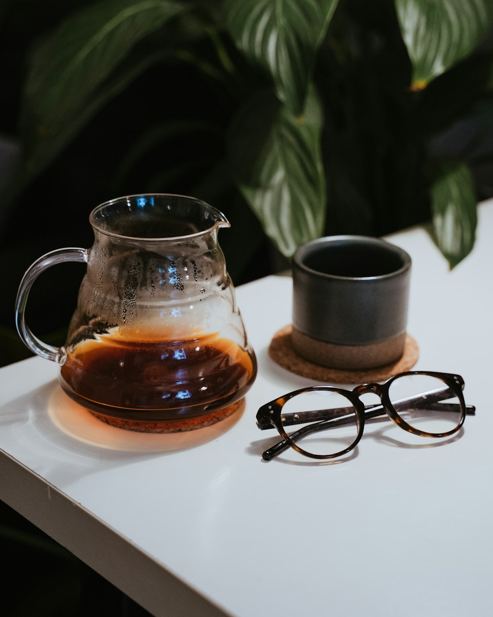 black framed eyeglasses beside clear glass mug on white table