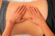Hands are applying gentle pressure on a person's back, indicating a massage or physical therapy session. The person is lying down and wearing a gray garment.
