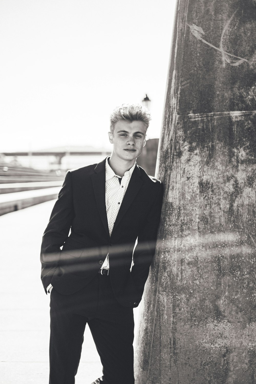 man in black suit jacket standing beside concrete wall