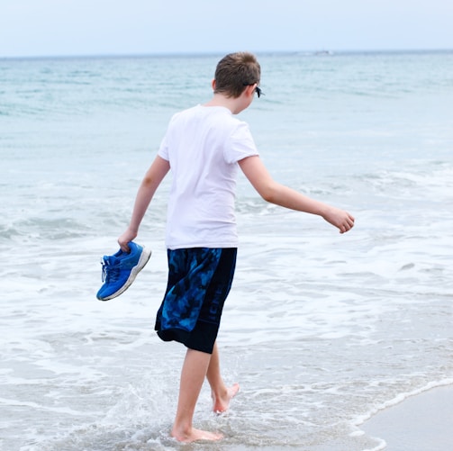 boy in white t-shirt and blue shorts running on beach during daytime