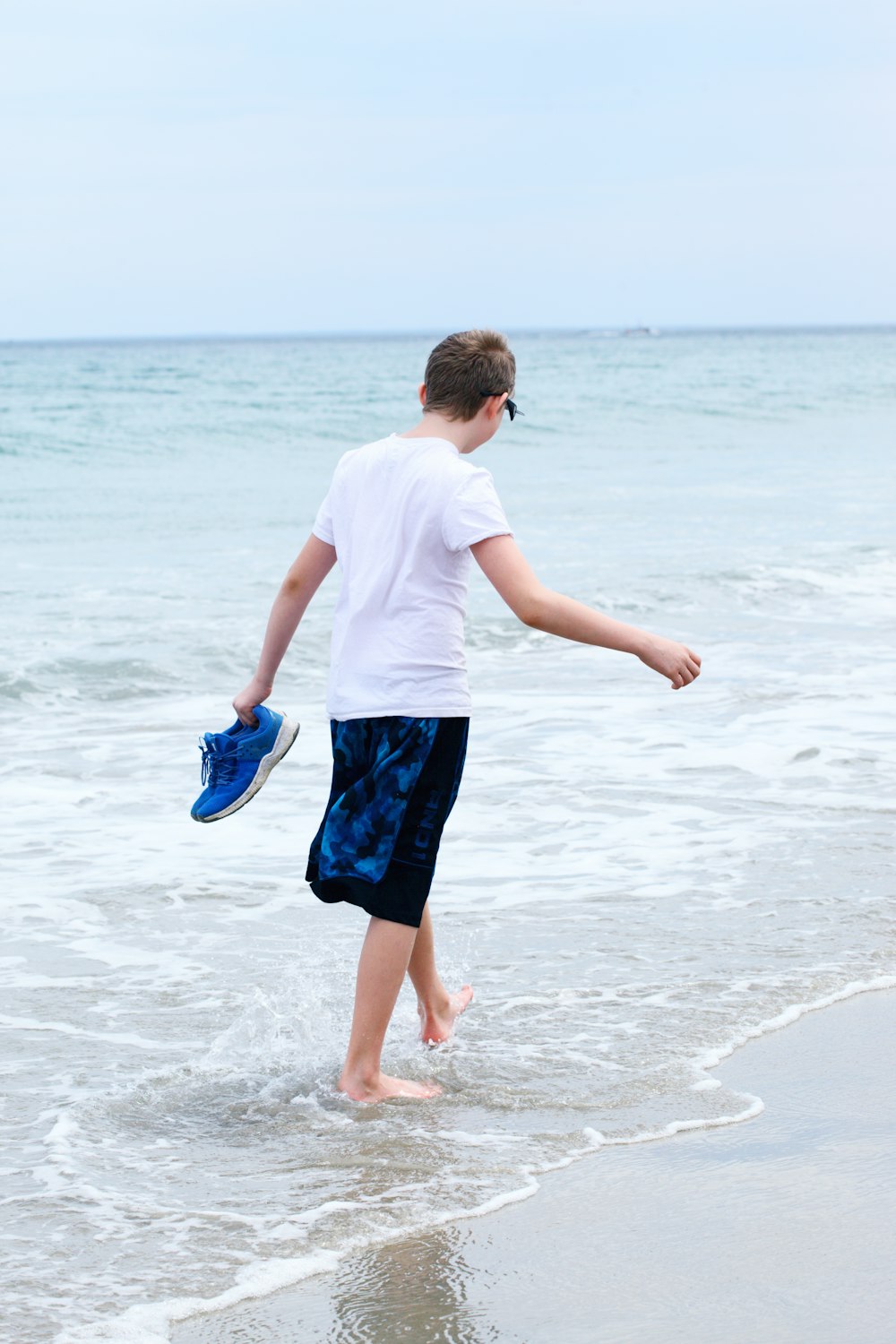 menino na camiseta branca e shorts azuis correndo na praia durante o dia