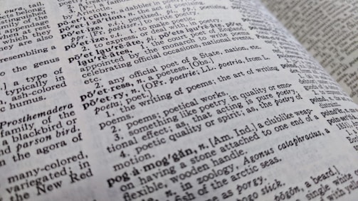 A close-up view of an open dictionary showing definitions related to poetry. The text is in black and white, with some words bolded for emphasis. The page curvature is slightly visible, indicating the book is laid open at an angle.
