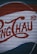 A section of a corrugated metal surface is painted with large red letters and a distinct logo design, possibly resembling vintage signage or advertising artwork.