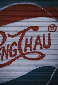 A section of a corrugated metal surface is painted with large red letters and a distinct logo design, possibly resembling vintage signage or advertising artwork.
