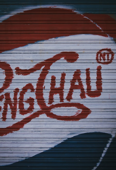 A section of a corrugated metal surface is painted with large red letters and a distinct logo design, possibly resembling vintage signage or advertising artwork.