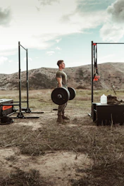 A fit man lifting weights outdoors with a bright morning sun.