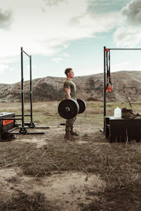A fit man lifting weights outdoors with a bright morning sun.
