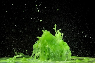 Vibrant green liquid splashes dynamically against a dark background, creating an energetic and lively scene.