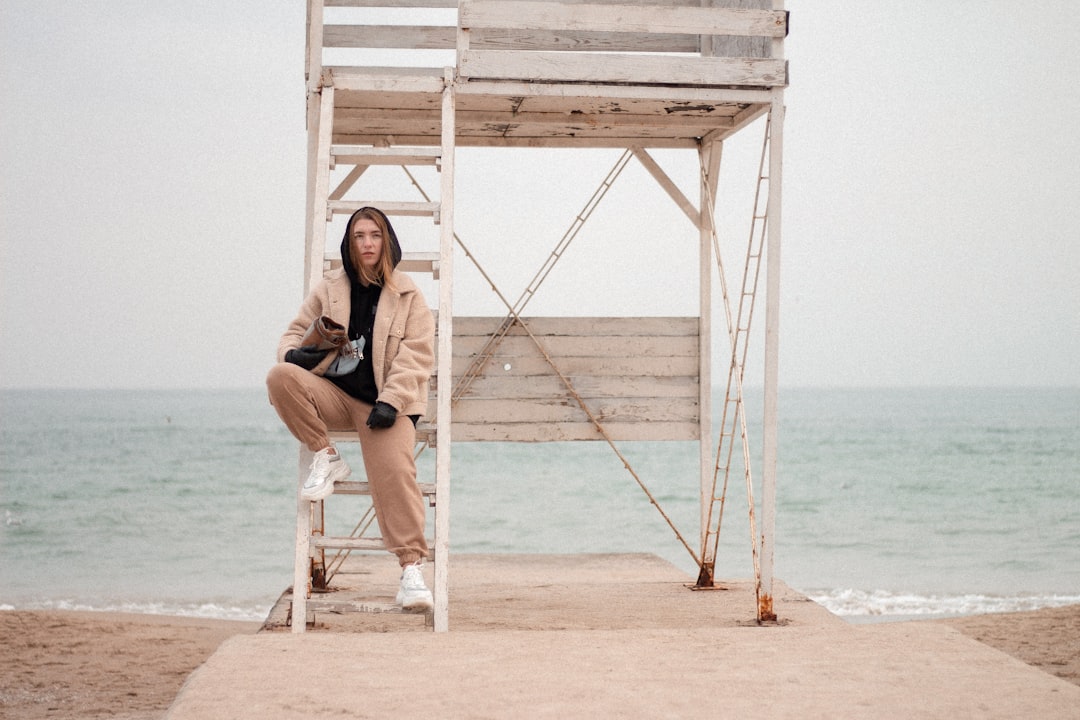 woman in black shirt sitting on white wooden ladder on beach during daytime