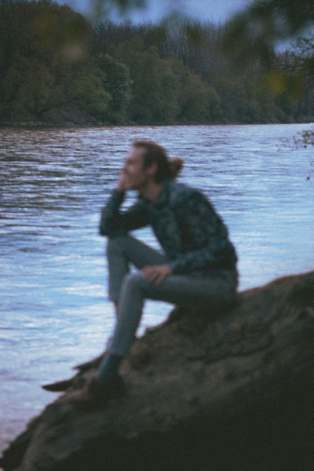 woman in black jacket and gray pants sitting on rock near body of water during daytime