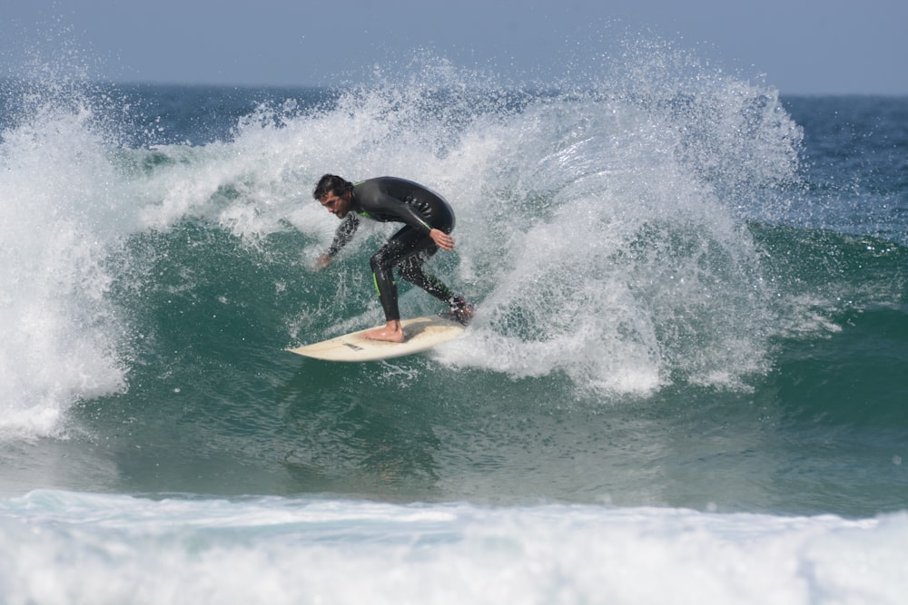 Hombre con traje de neopreno negro surfeando sobre las olas del mar durante el día