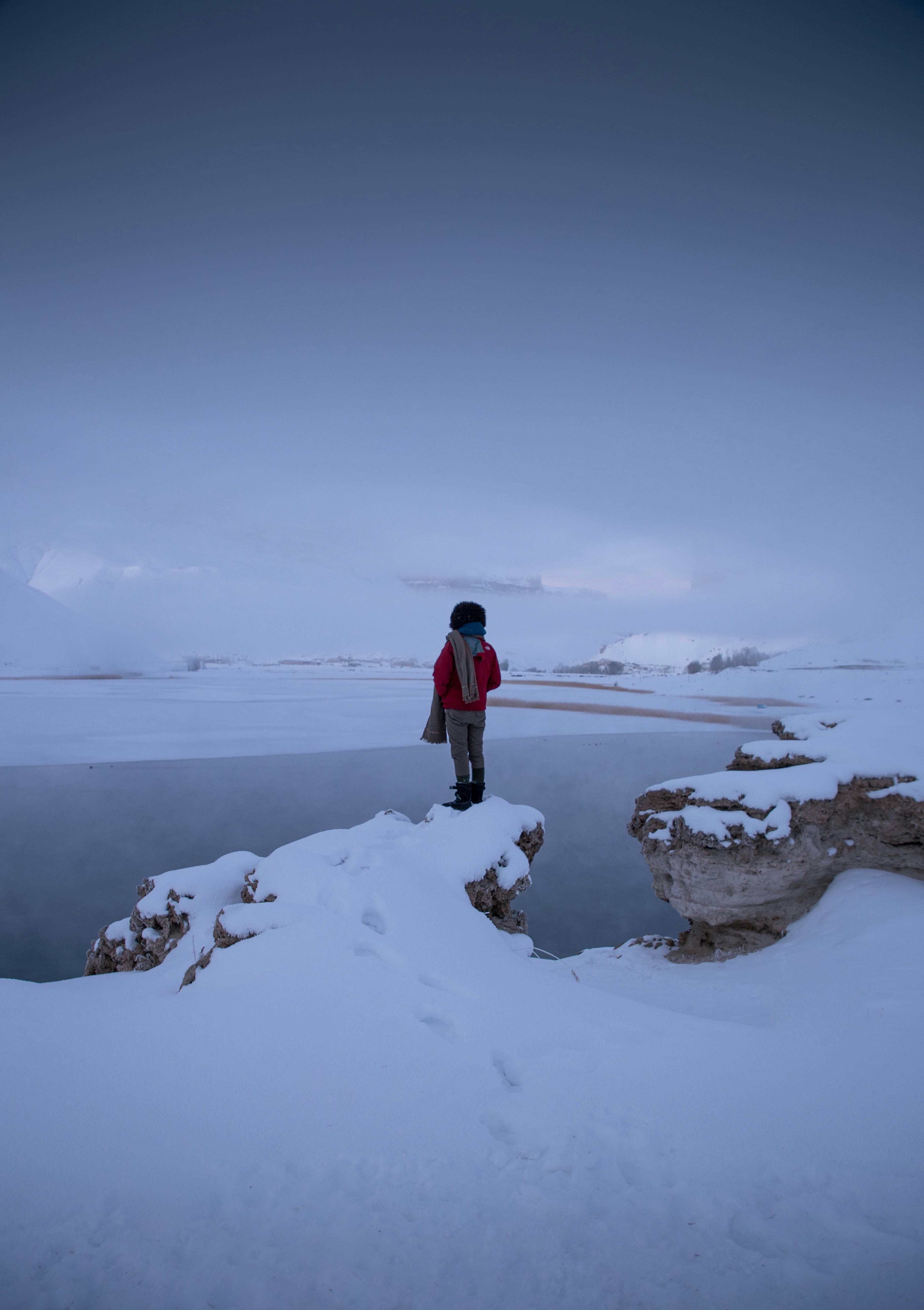 man in red jacket standing on snow covered ground during daytime