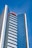 A tall modern skyscraper with many windows reflecting the blue sky. The building has a sleek, glass facade and is labeled with the red letters 'AON' near the top. The architecture is sharp and geometric, creating a sense of height and modernity.