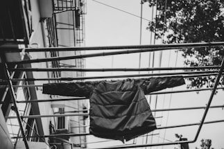 A close-up of a rugged, weatherproof jacket hanging on a hook with cityscape blurred in the background.