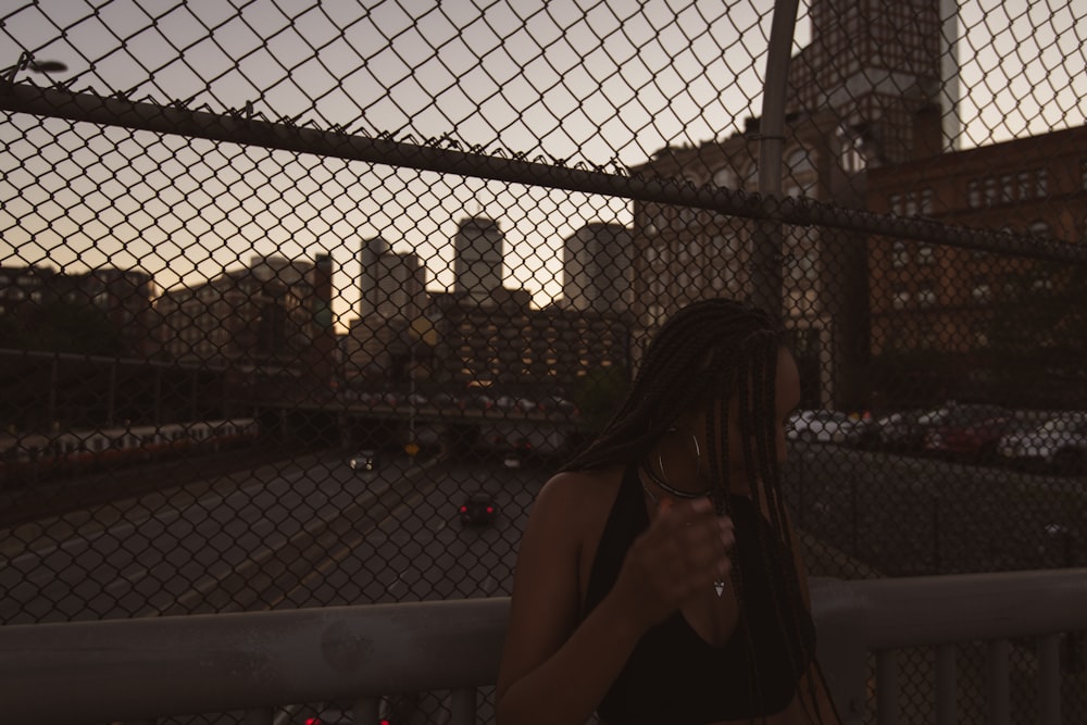 woman in black tank top leaning on gray metal fence during night time