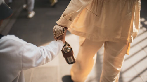 An authentic moment of a child holding hands with parents, bathed in soft sand-colored light.