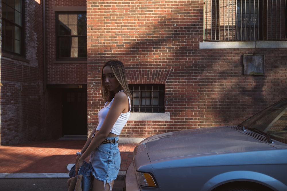 woman in white tank top and blue denim jeans leaning on black car