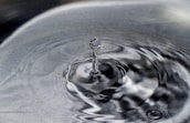 A serene water droplet creating ripples on a polished silver surface.