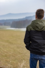 man in black jacket and blue denim jeans standing on green grass field during daytime