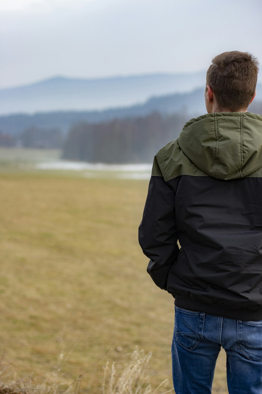 man in black jacket and blue denim jeans standing on green grass field during daytime