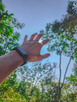 Wrist wearing the smartwatch while jogging along a tree-lined path, sunlight filtering through leaves.