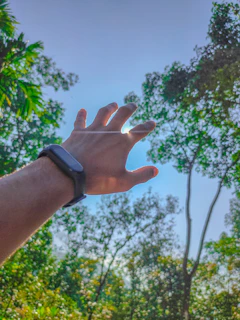 Wrist wearing the smartwatch while jogging along a tree-lined path, sunlight filtering through leaves.