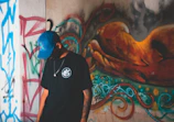Model wearing a red and black graphic tee paired with a matching cap against an urban graffiti wall.