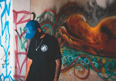 Model wearing a red and black graphic tee paired with a matching cap against an urban graffiti wall.