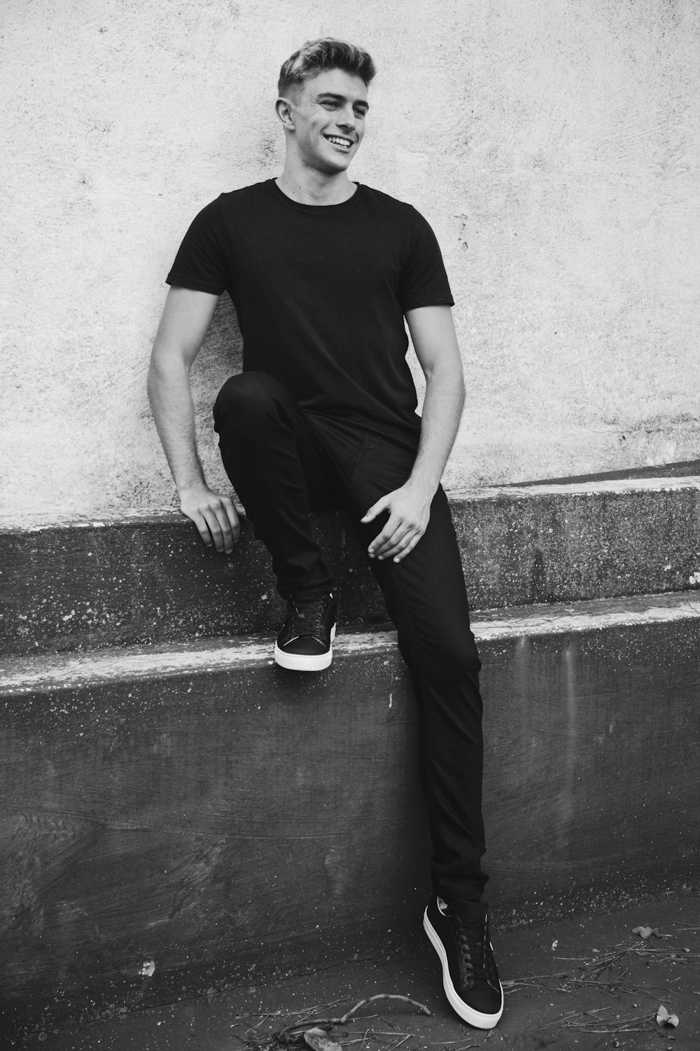 man in black crew neck t-shirt and black pants sitting on concrete wall