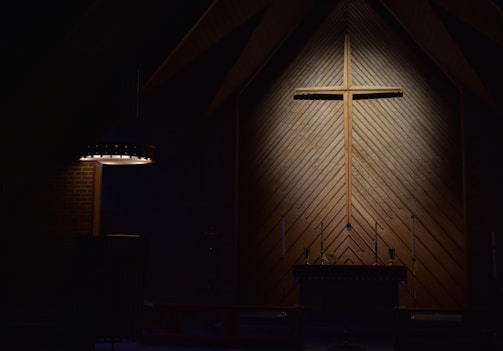 A close-up of a wooden cross hanging against a bright yellow wall.
