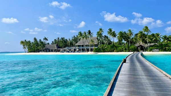 A wooden pier leading to a tropical island resort with palm trees and beach — Maldives, Maldives
