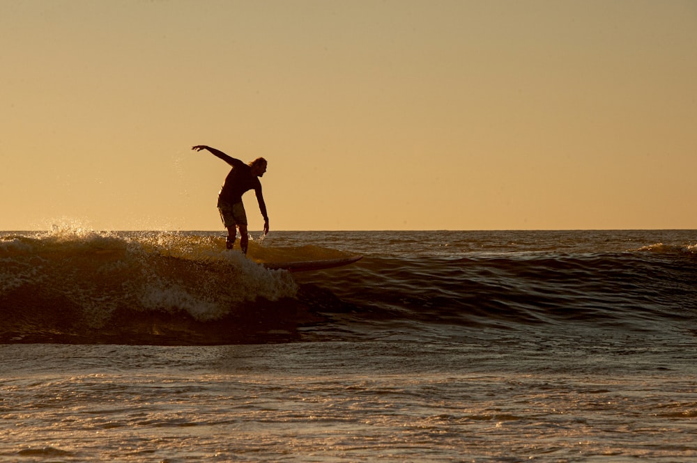 hombre en pantalones cortos negros surfeando en el mar durante el día