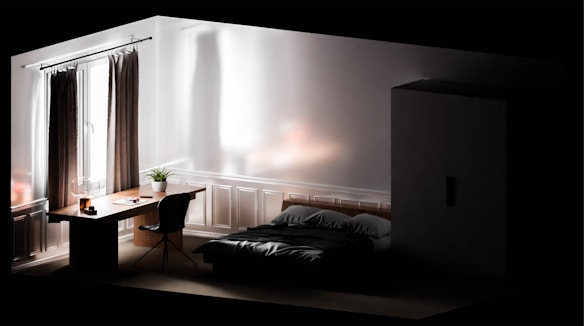 A minimalist bedroom with a modern aesthetic. It features a bed with dark bedding, a wooden desk with a plant and lamp, a chair, a wardrobe, and a large window with curtains. The room is softly lit, creating a serene atmosphere.