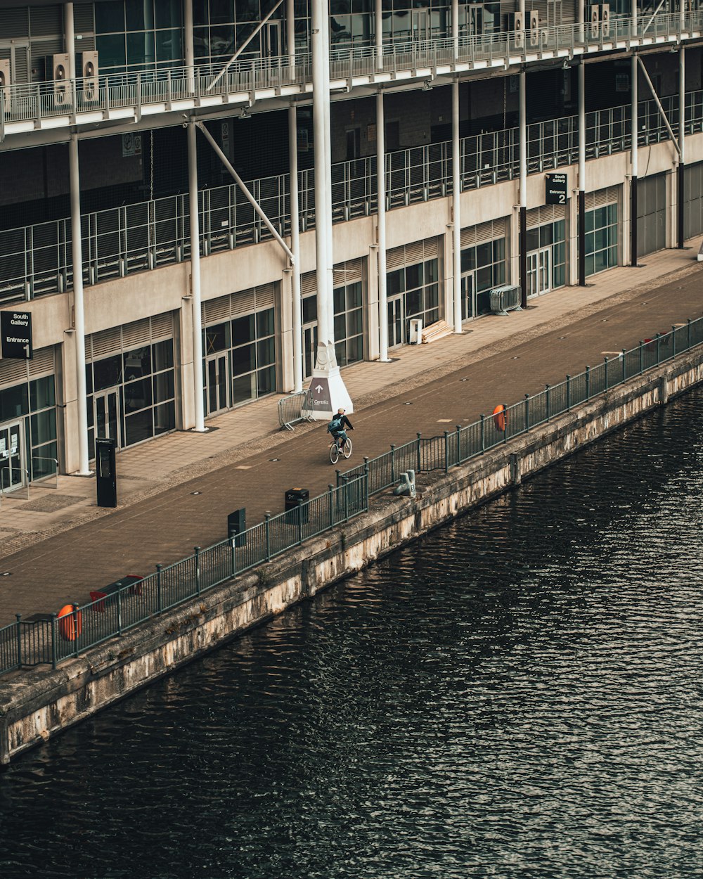 man in white shirt and black pants walking on sidewalk near body of water during daytime